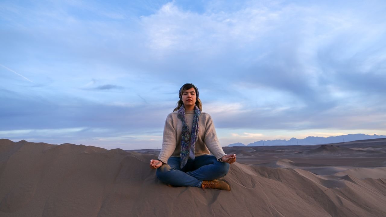 Woman meditating in a calm desert landscape at sunset in Yazd, Iran.