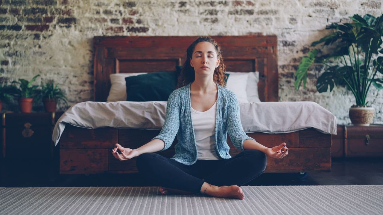 Woman practicing meditation in a calm bedroom setting, promoting relaxation and mindfulness.