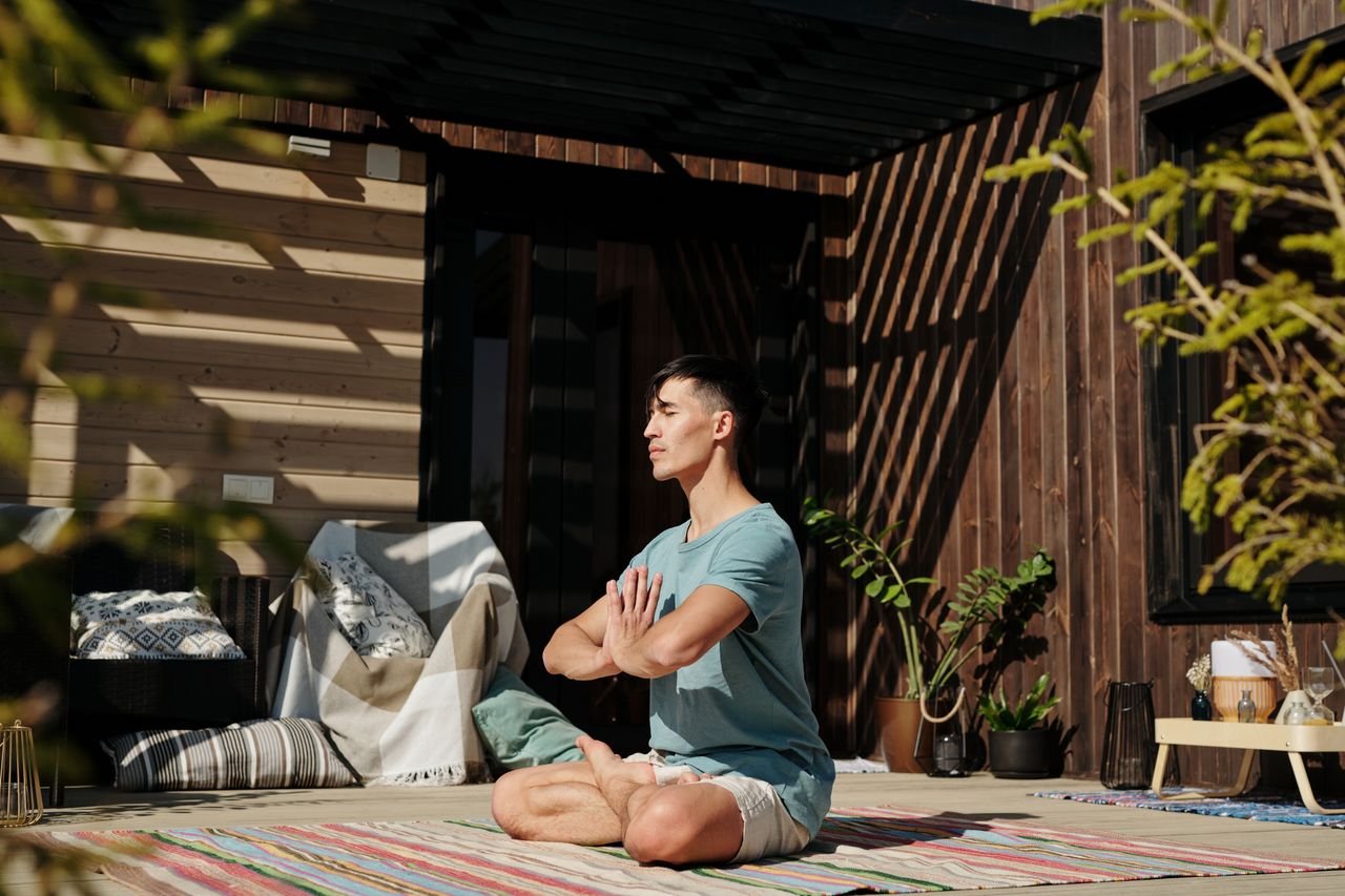 ours-journey Man practicing yoga meditation on a sunny spring day, surrounded by nature on a wooden deck.